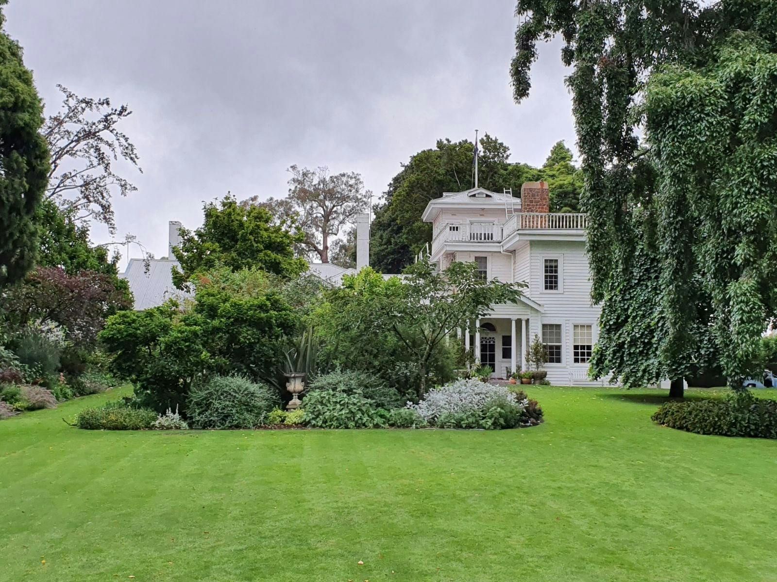 Lush garden lawn before a white house with balconies and tall trees