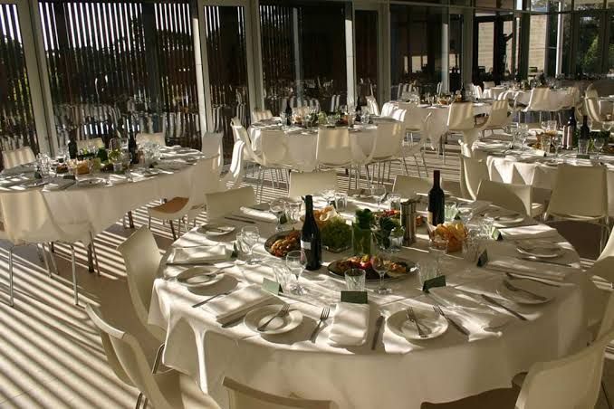 Elegant banquet hall with round, set tables, white linens, and sunlight through tall windows