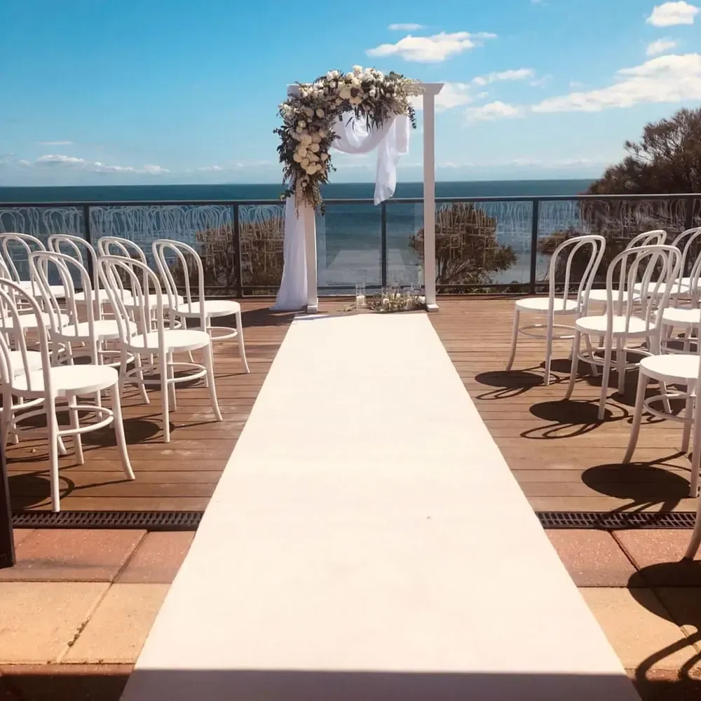 Outdoor wedding aisle with white chairs and floral arch overlooking the ocean