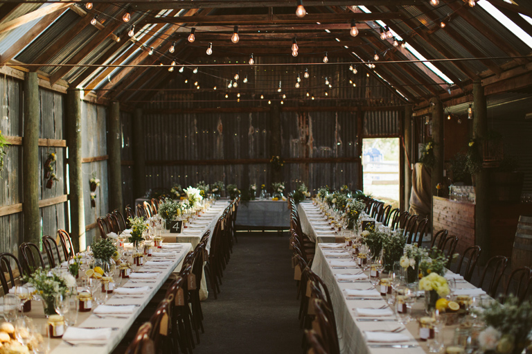 Rustic barn wedding reception setup with long tables, flowers, and string lights