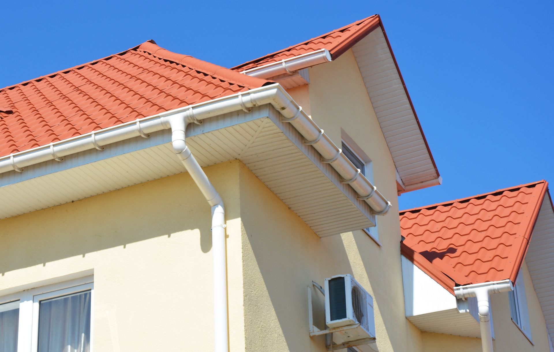 Cream-colored house exterior with red tiled roof and white gutters against a blue sky