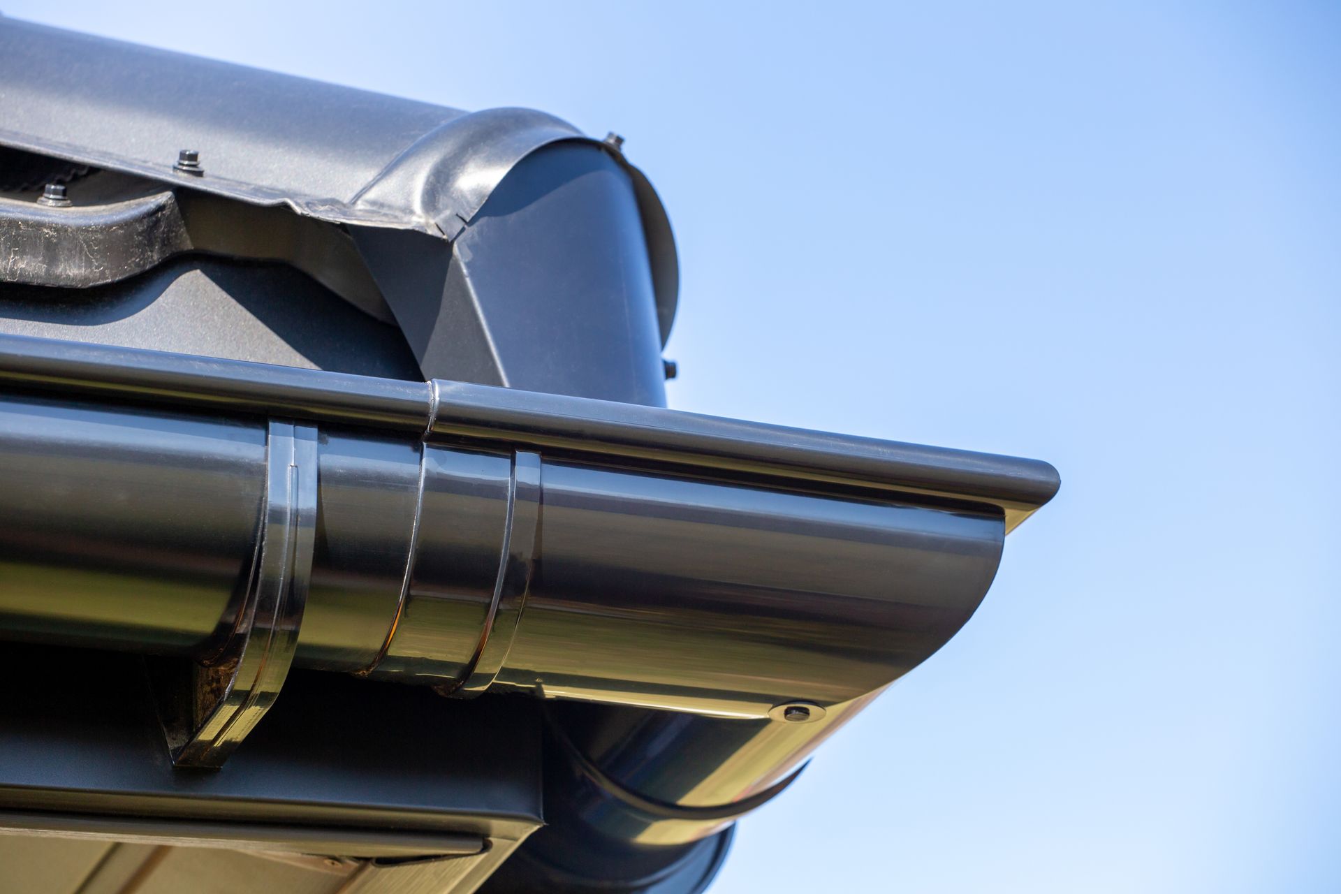 Close-up of a silver roof gutter and downspout against a blue sky