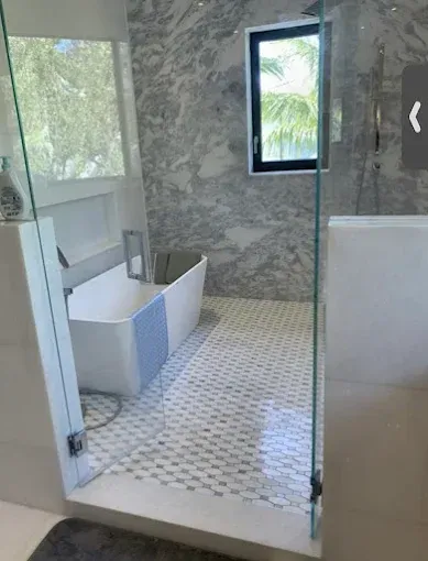 Modern bathroom with walk-in shower, white tub, mosaic tile floor, and windows letting in daylight