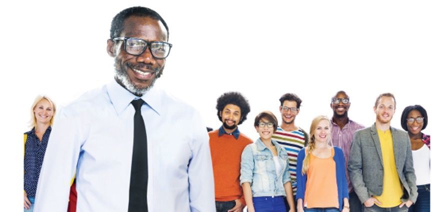Group of diverse people smiling, with a man in the foreground wearing a dress shirt and glasses.