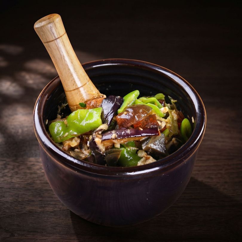 Black bowl with a wooden spoon holding a vegetable dish on a dark table
