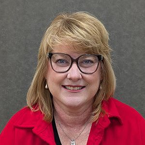 Woman with blonde hair, wearing glasses and red shirt, smiling at camera.