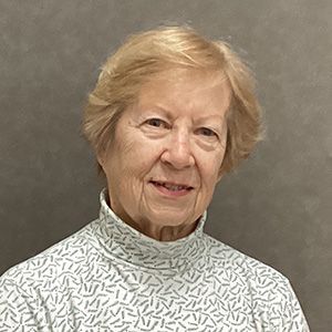 Woman with short blonde hair, smiling, wearing a patterned turtleneck sweater, set against a plain backdrop.