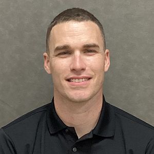 Man in black collared shirt smiling, facing the camera.