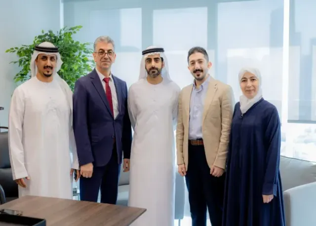 Five people pose indoors. Men in suits and traditional Arab attire.