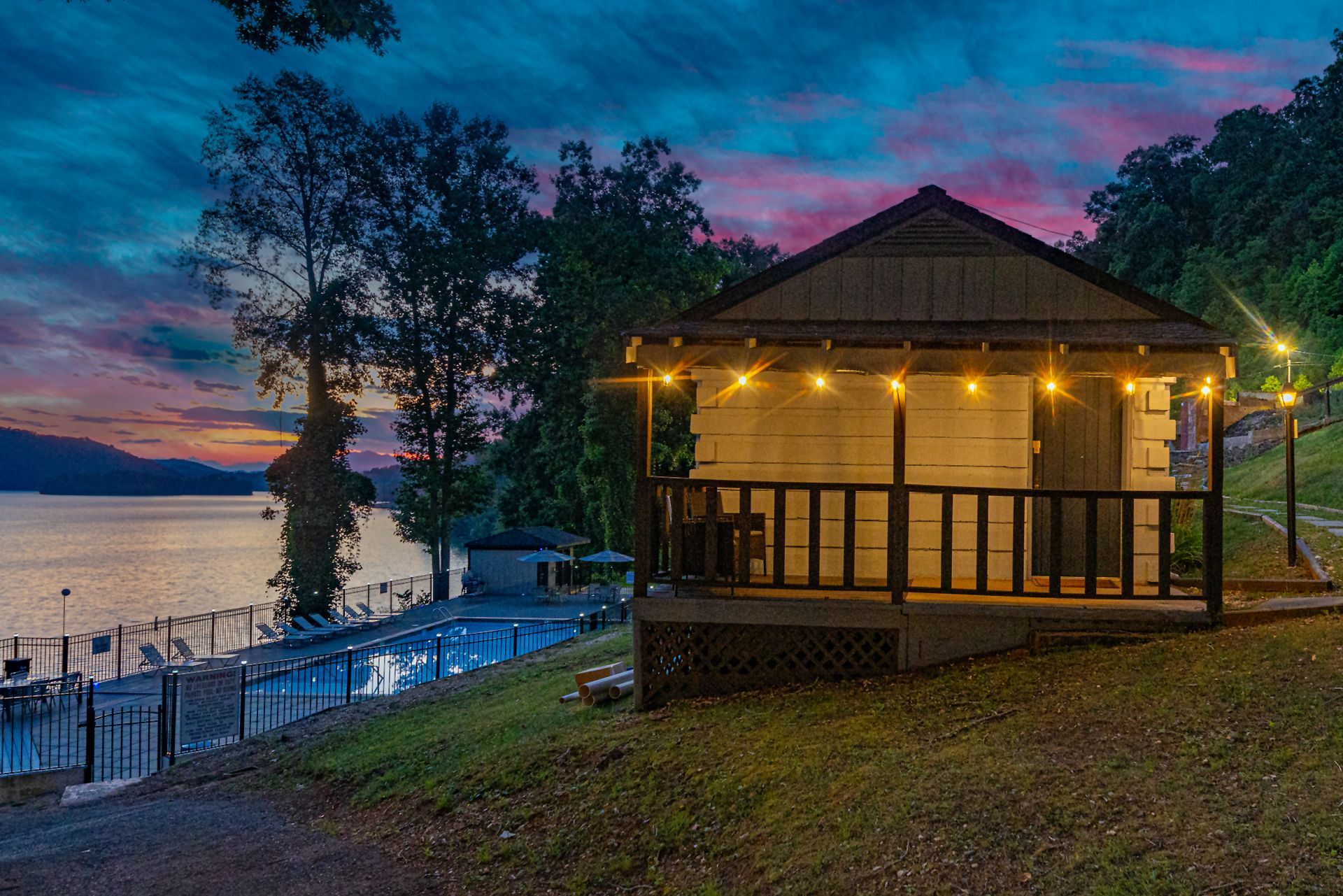 Lakeside cabin with string lights at dusk, with the pool and lake behind it