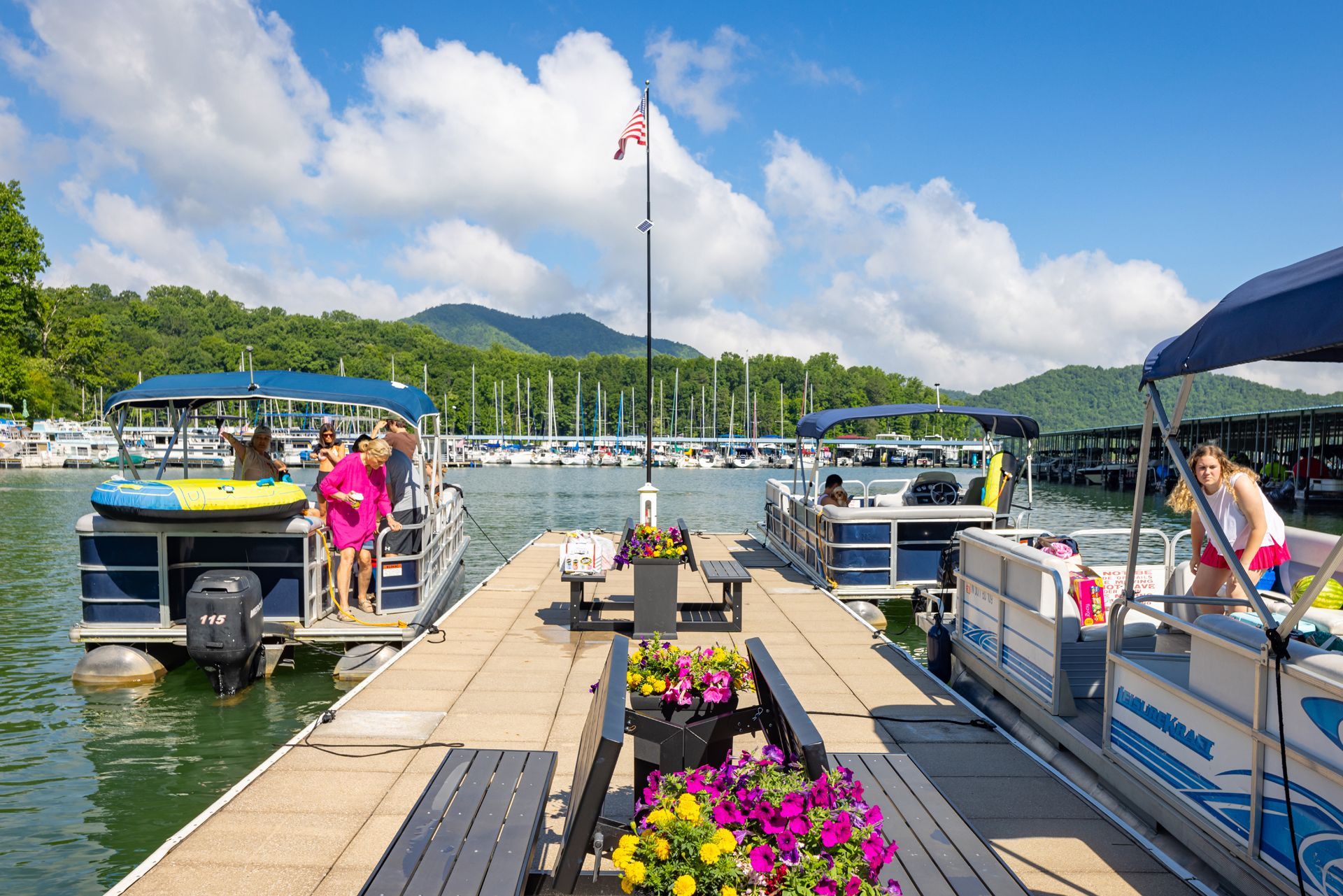 Pontoon boats and guests at a flower-lined dock on the lake