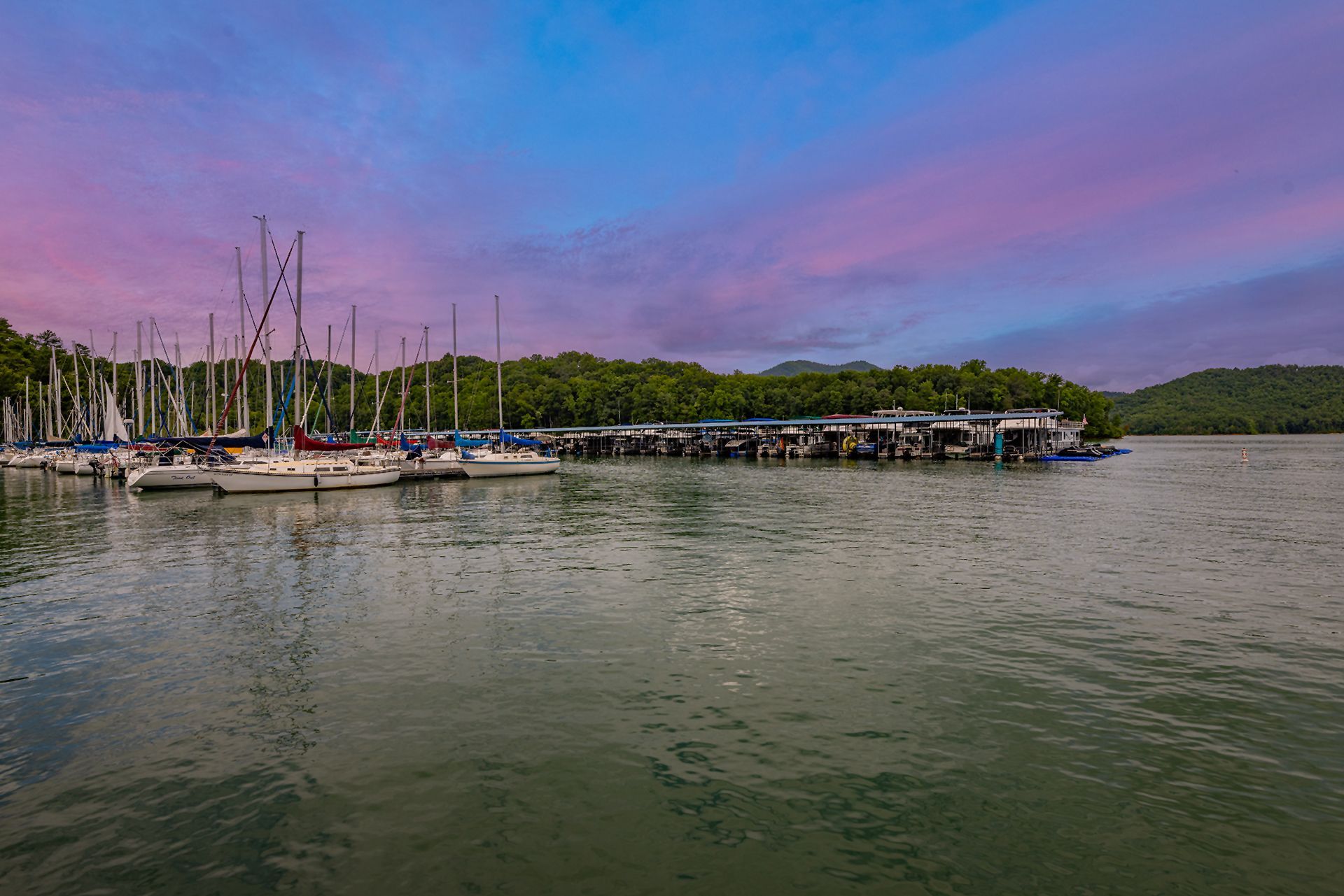 Sailboats and covered docks along the shore at dusk under a pink and purple sky