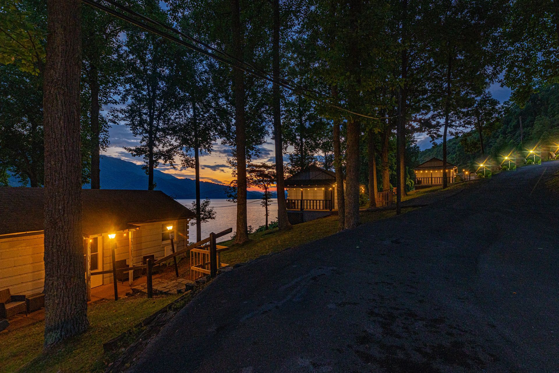 Lakeside cabins with lights glowing at dusk among tall trees