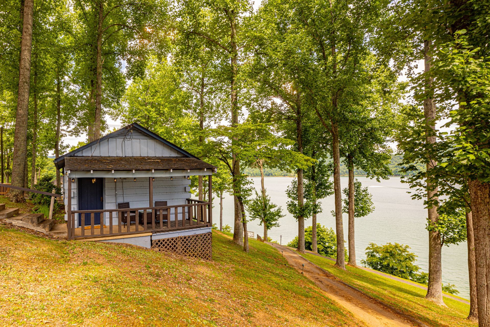 Small cabin with a front porch among trees, overlooking the lake