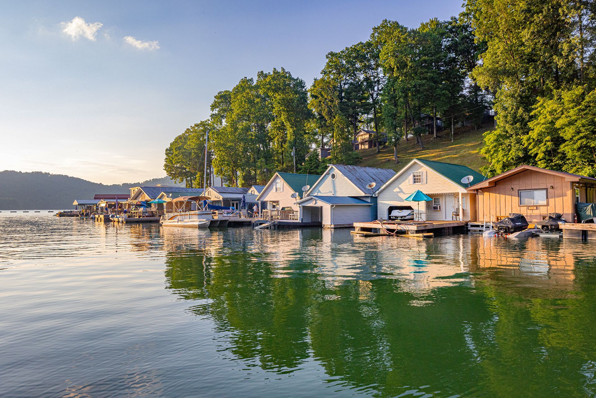 Row of waterfront boathouses on a calm lake, with trees behind