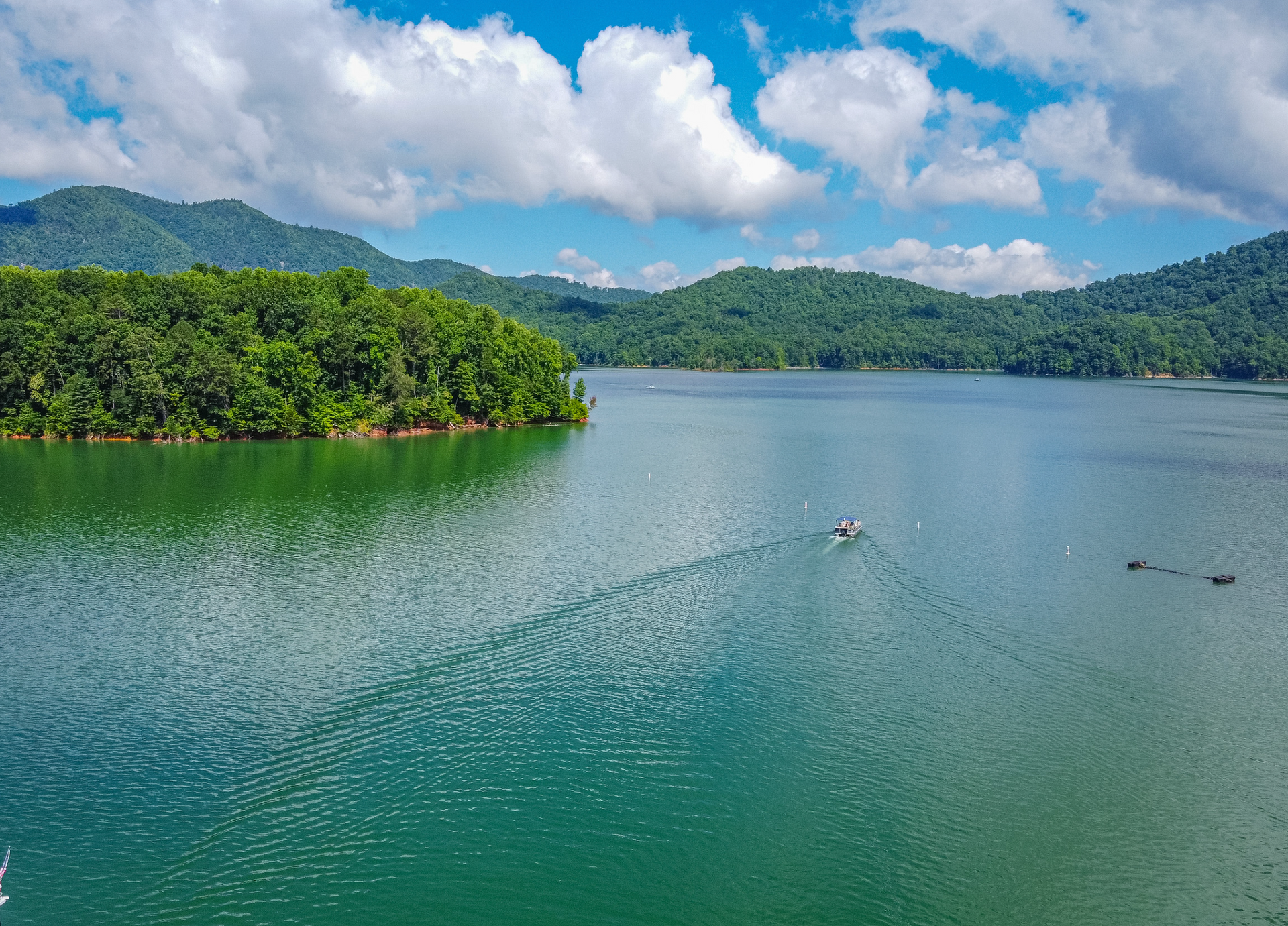 Small boat on a calm lake surrounded by forested hills under a blue sky