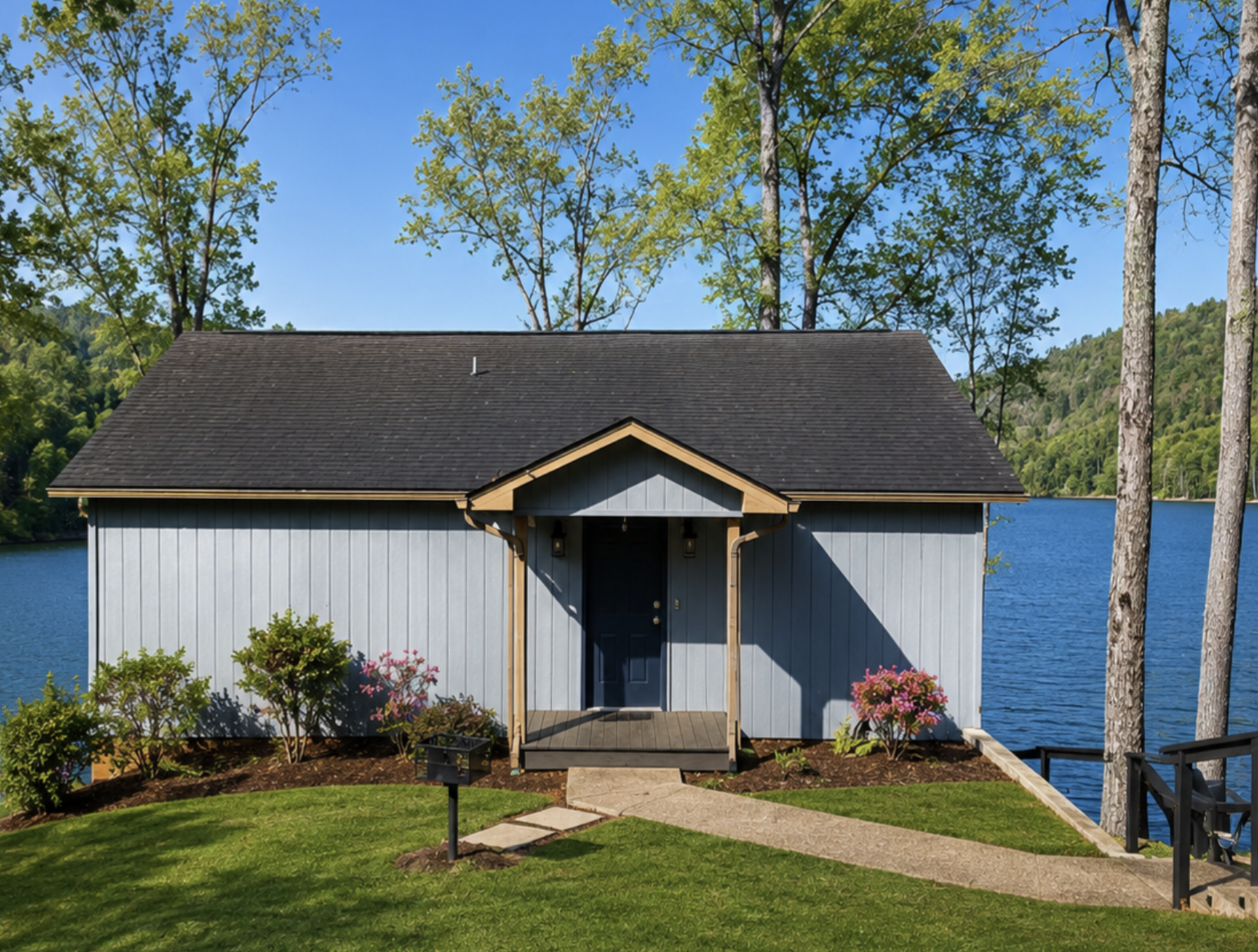 Gray lakeside cottage with a covered entry, with trees and water behind