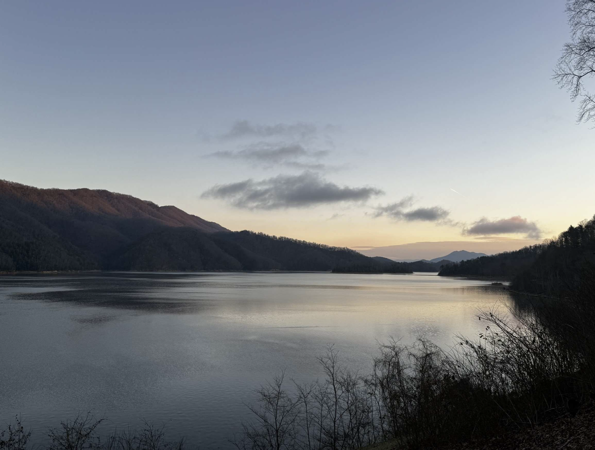 Calm lake at dusk, with dark hills and wispy clouds in a pale sky