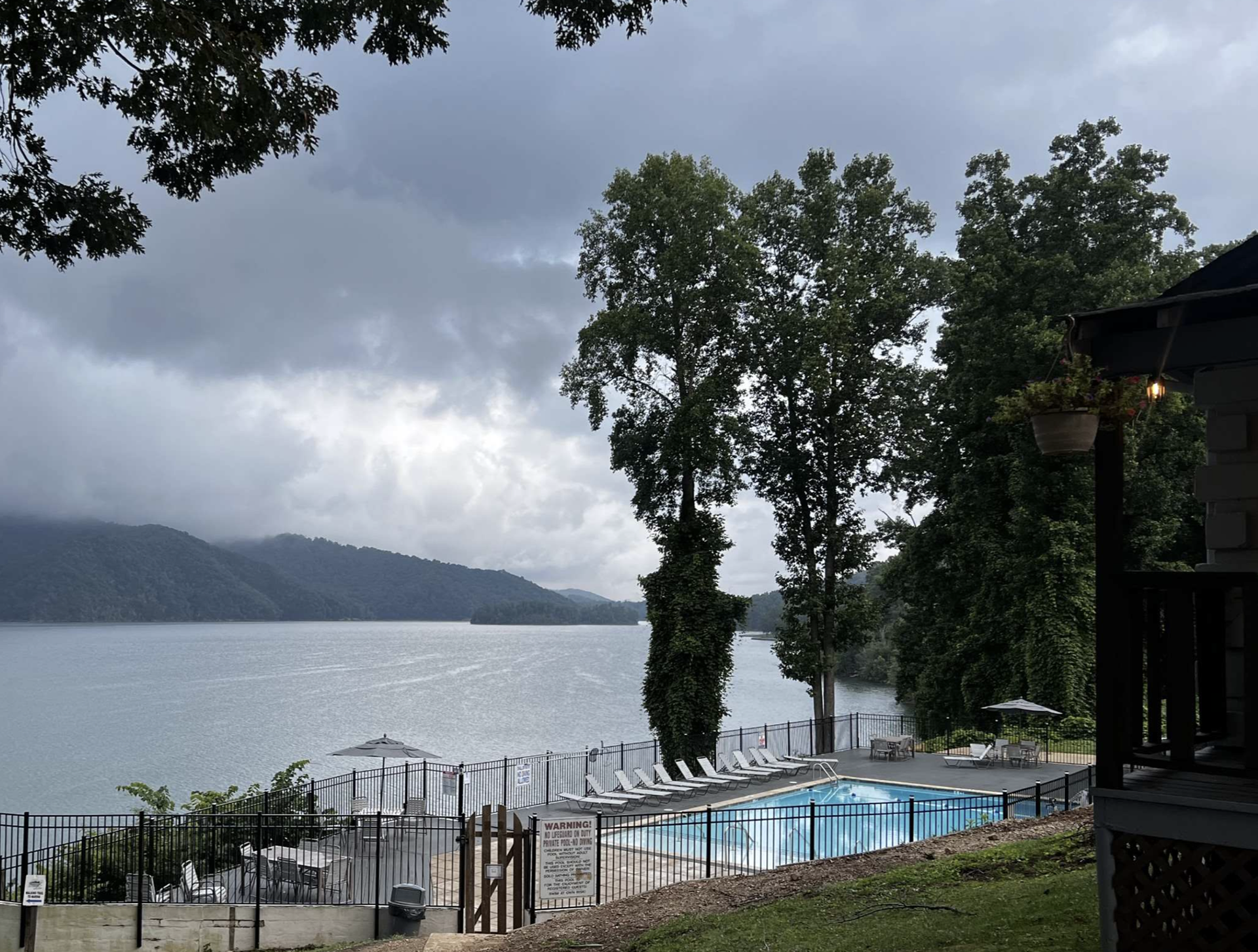 Lake view under cloudy skies, with tall trees and a covered porch on the right
