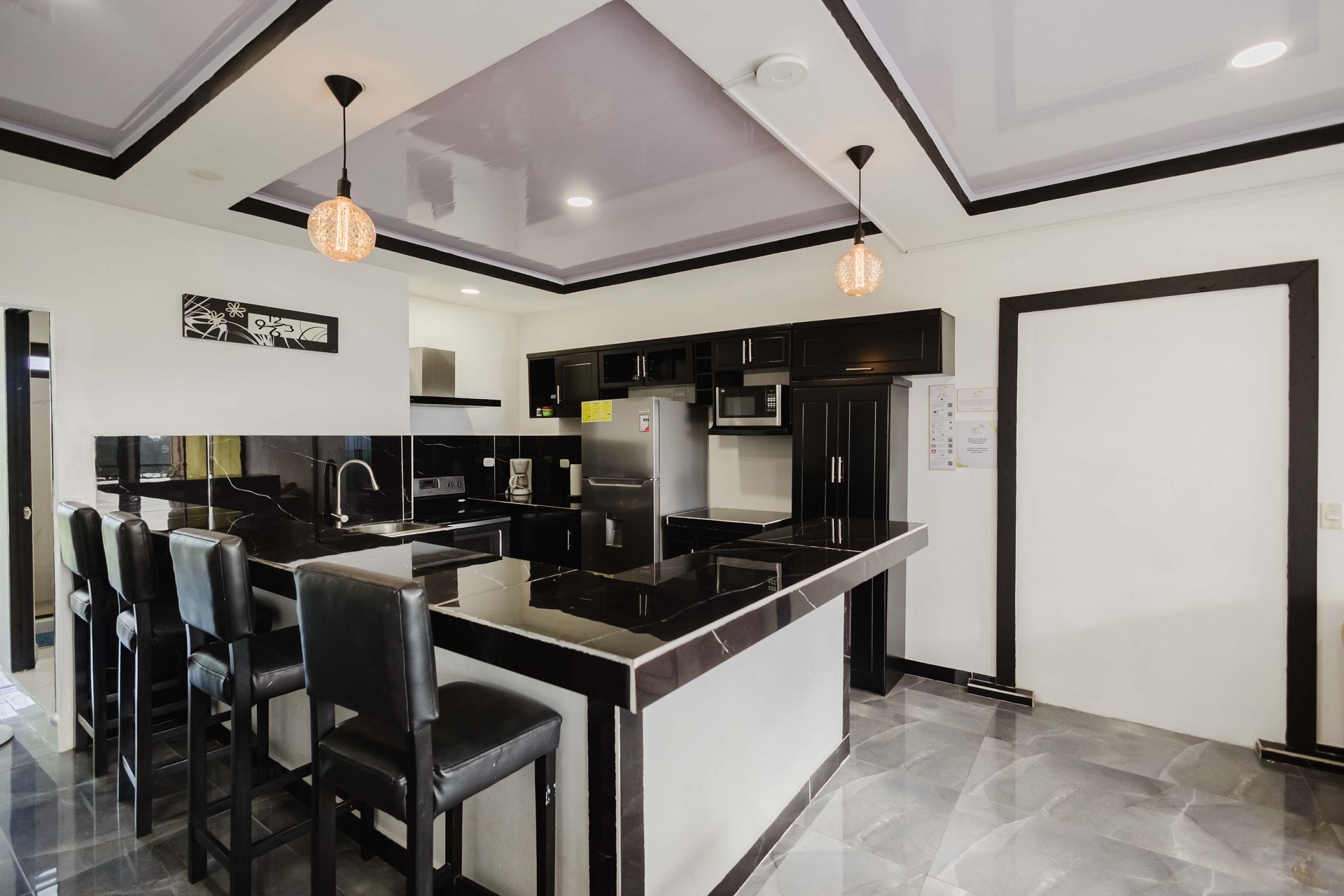 Cocina moderna con electrodomésticos negros, isla de mármol blanco y dos taburetes blancos.