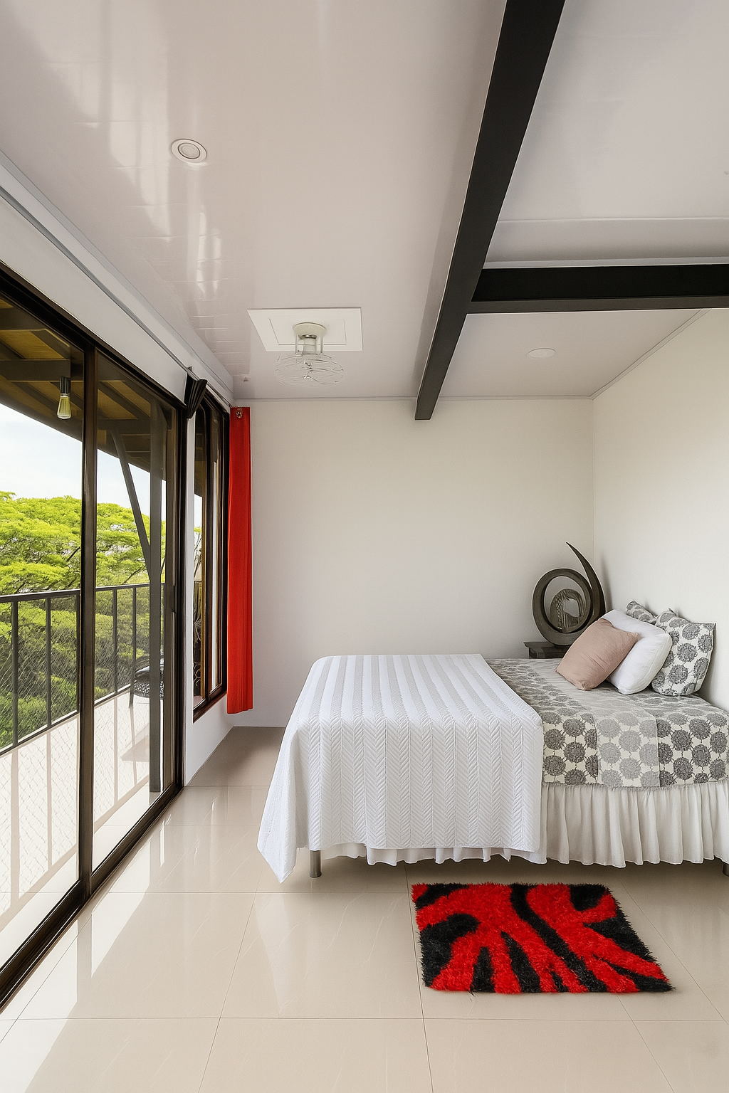 Habitación luminosa y moderna con cama individual, alfombra roja, puertas correderas de cristal y balcón con vistas.