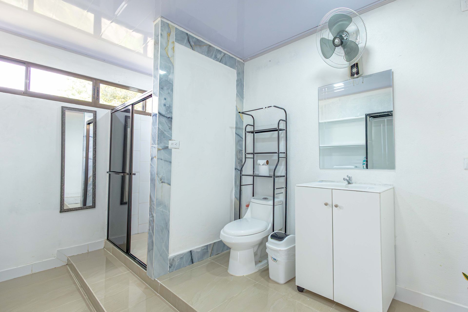 Baño luminoso con ducha, inodoro, lavabo con mueble, espejo y luz de ventana.