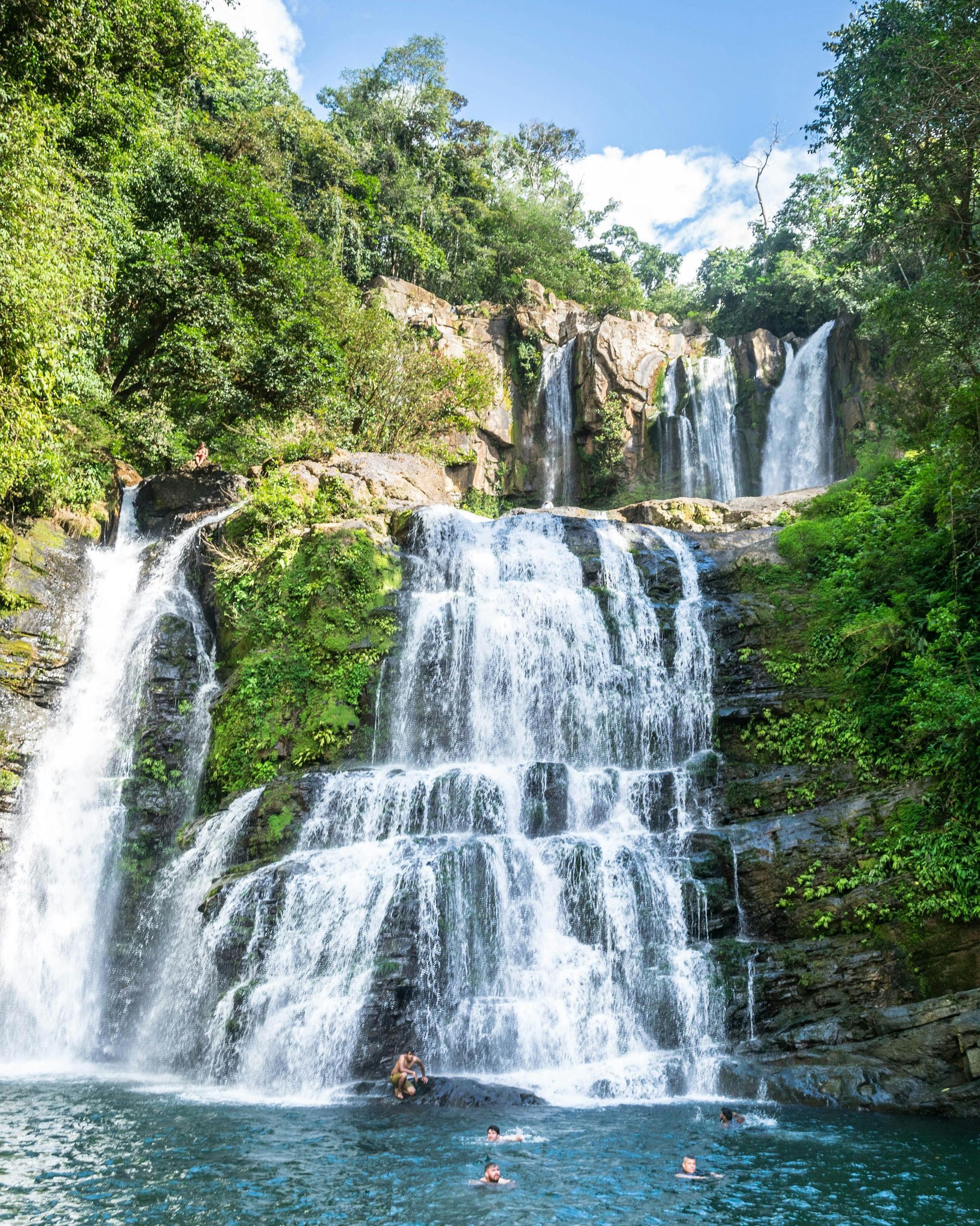 Una cascada en medio de un bosque con gente nadando en ella.