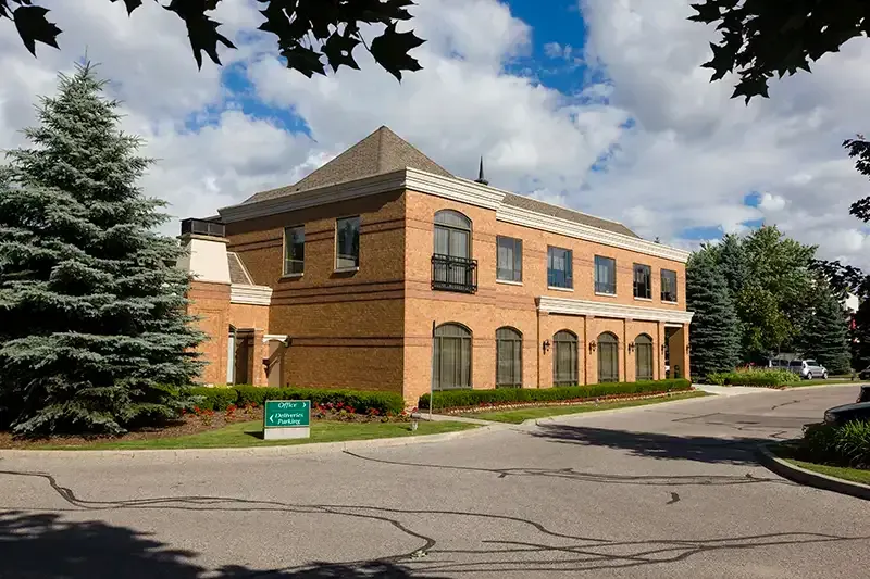 Two-story brick building with arched windows. Green trees and blue sky in the background.