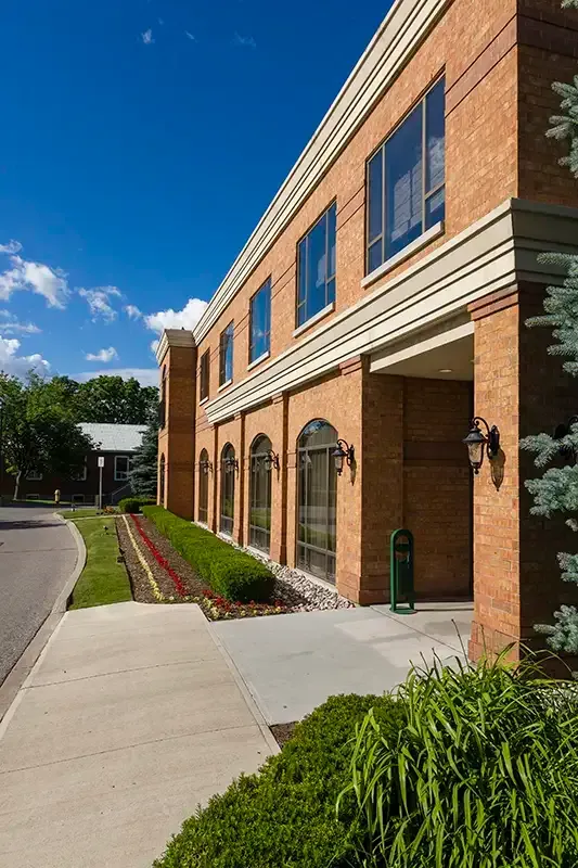 Brick building with windows, sidewalk, landscaping, and blue sky.