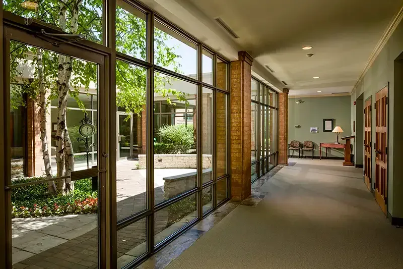 Hallway with large windows looking onto a courtyard with trees, brick columns, and a waiting area.