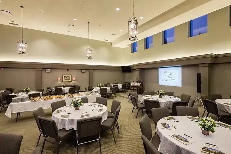 A banquet hall with round tables set for a gathering, food on a buffet table, and a projected image.