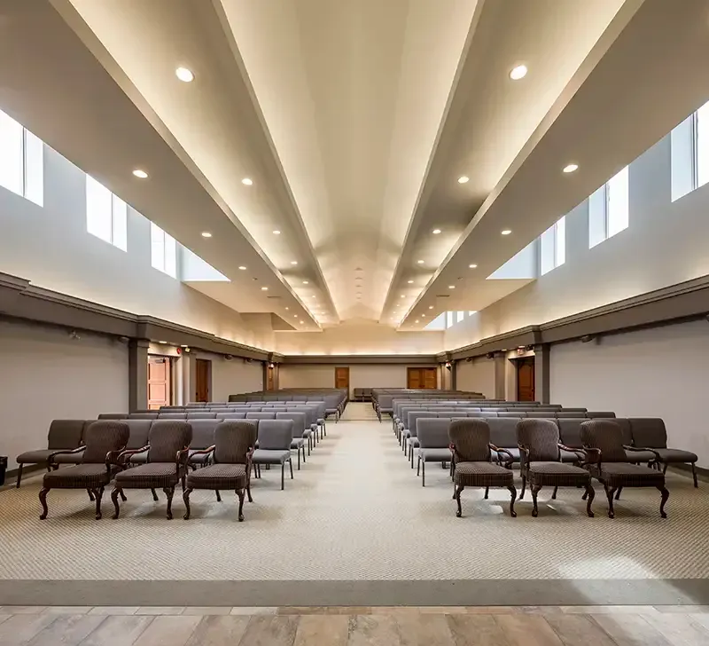 An empty chapel with rows of chairs, skylights, and neutral colors.