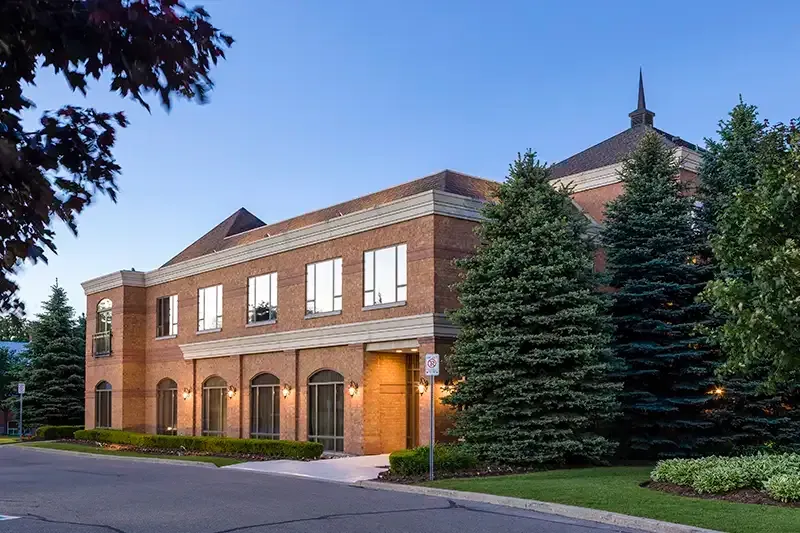 Brick office building with arched windows, set on a well-maintained lawn and trees.