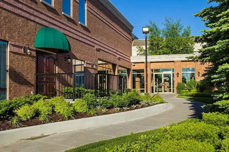 Brick building with green awning, walkway, greenery, and a blue sky.