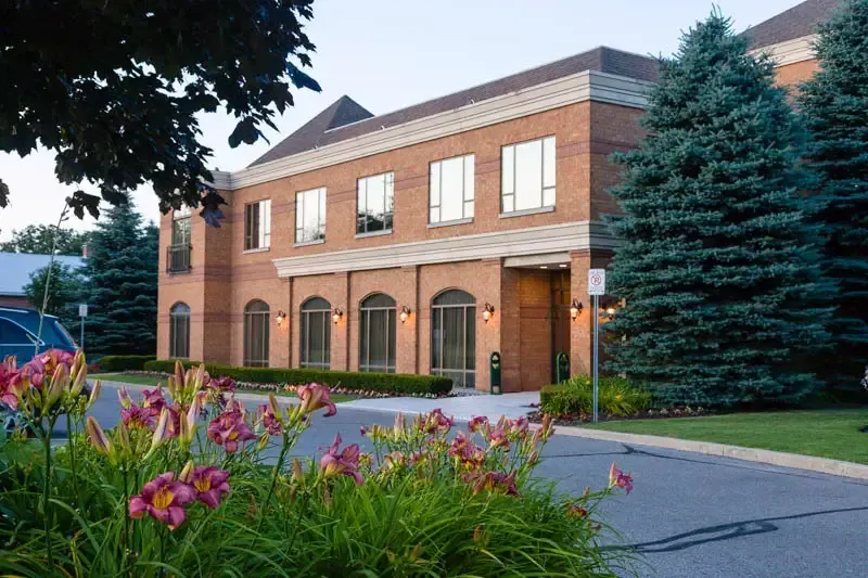 Brick building with arched windows and a landscaped driveway, flowers in foreground.