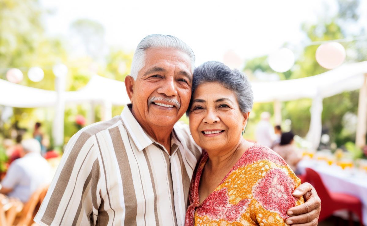 Smiling elderly couple embracing outdoors at a gathering.