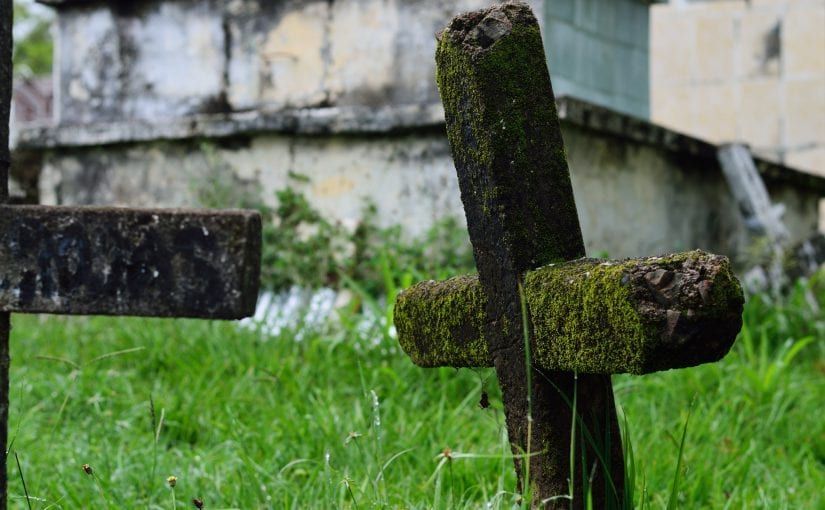 Stone crosses, covered in moss, in a grassy cemetery.
