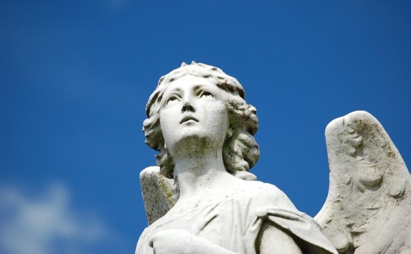 Stone angel statue looking upwards against a bright blue sky.