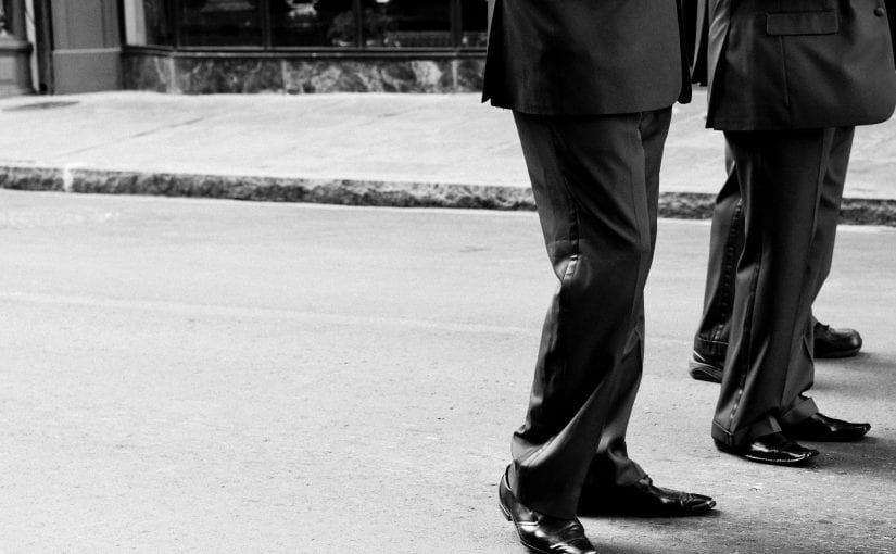 Two people in dark suits standing on a city street. Black and white photo.
