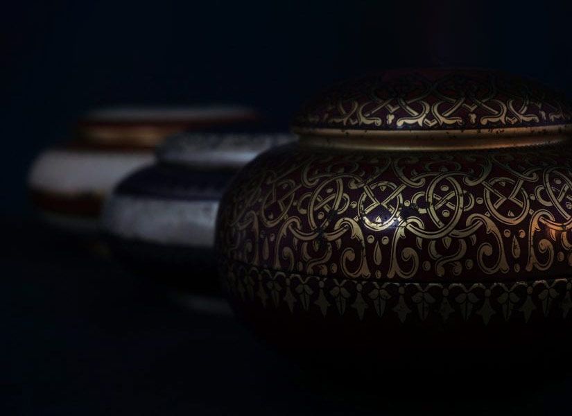 Three ornate, lidded jars in a row; dark red jar in front with gold design, fading to white and blue jars.