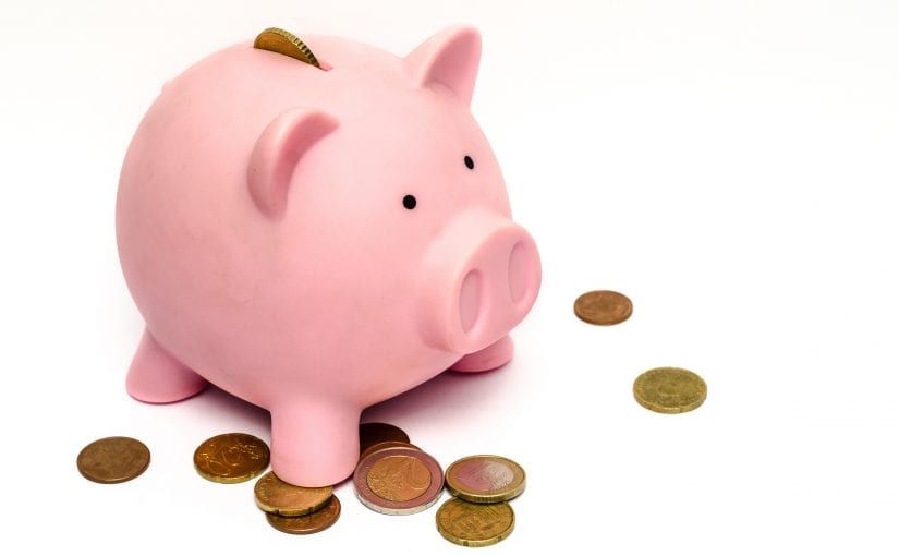 Pink piggy bank with coins scattered around it.