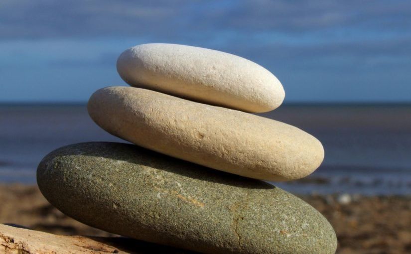 Three smooth stones stacked on each other, near the water; a symbol of balance and harmony.