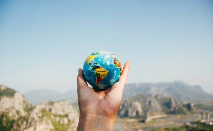 Hand holding a globe, mountains in the background, blue sky.