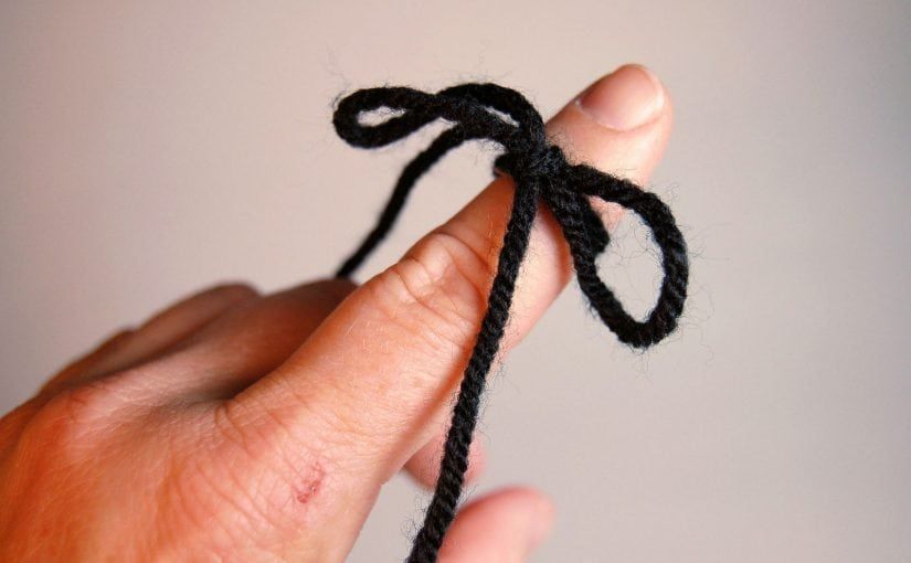 Hand with black yarn tied in a knot around a finger.