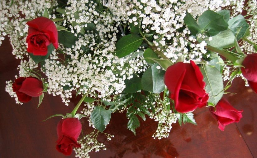 Red roses nestled among white baby's breath, on a glossy brown surface.