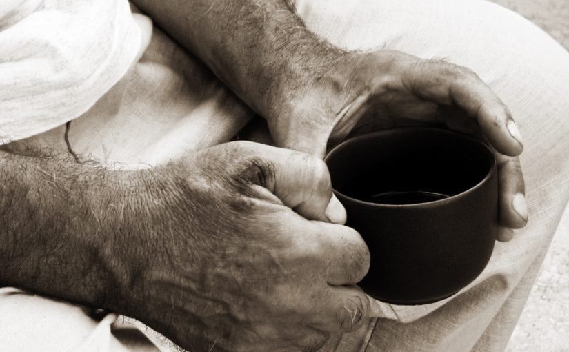 Man's hands holding a dark mug; sepia tone.