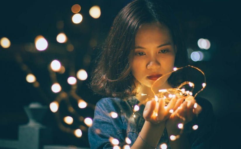 Woman holding string lights, glowing in the dark.