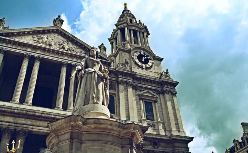 St. Paul's Cathedral, London, with a statue in the foreground, under a blue sky with clouds.