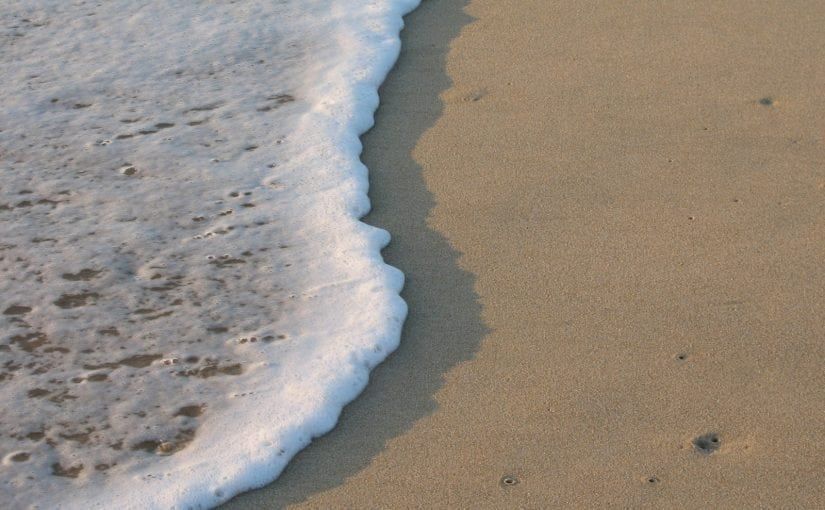 Foamy white ocean waves washing onto a sandy beach.