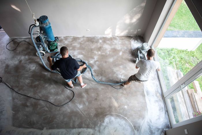two men are working on a concrete floor in a room with a concrete grinder.